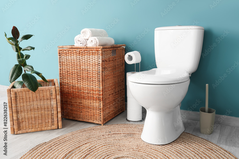 Interior of restroom with toilet bowl plant and basket near blue wall Interior of restroom with toilet bowl plant and basket near blue wall