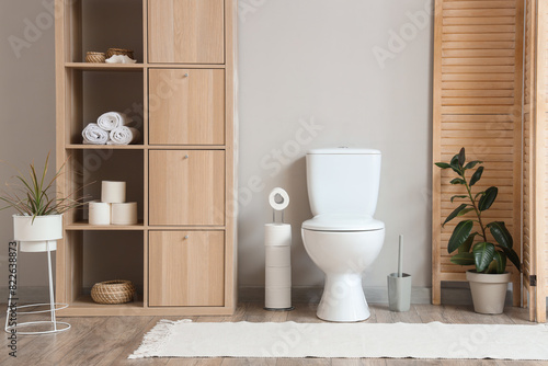 Interior of restroom with toilet bowl, closet and folding screen near grey wall
