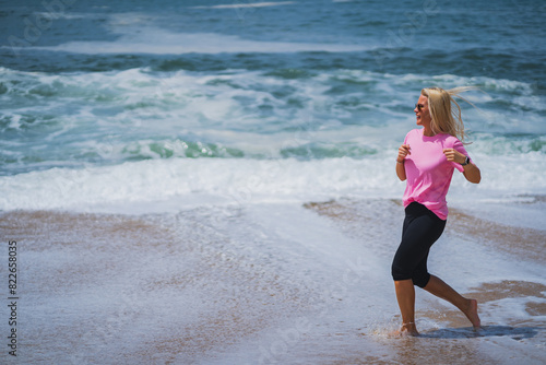 A young girl of European appearance in a pink T-shirt goes in for sports, running on the beach near the ocean. © Dmitri