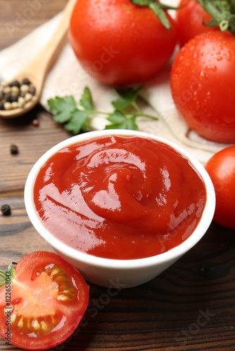 Delicious ketchup in bowl and tomatoes on wooden table, closeup
