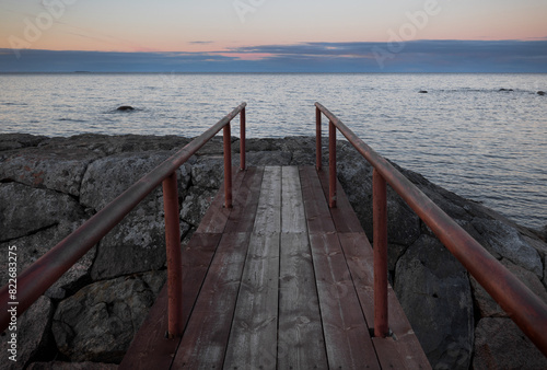 An old wooden bridge pier on the background of a beautiful sunset sky on the shore of the lake. Karelia, Russia.