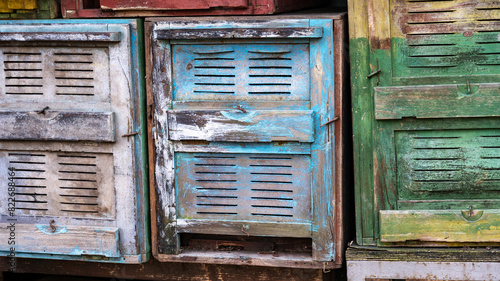 Old beehives featuring faded paint in blue green with peeling and chipping, rustic worn aesthetic. Aging, weathered look symbolizes passage of time and life cycle of in traditional apiculture practice