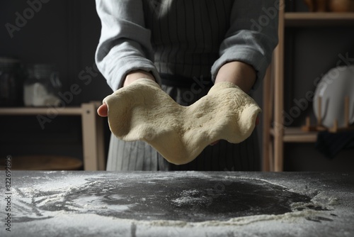 Woman tossing pizza dough at table in kitchen, closeup photo