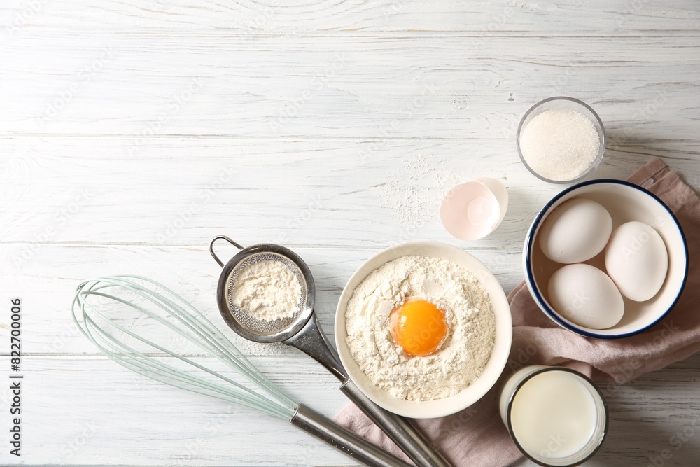 Flour with yolk in bowl and other ingredients for dough on white wooden table, flat lay. Space for text