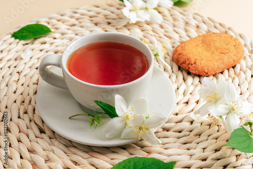 A cup of jasmine tea on a wicker place mat with jasmine flowers and biscuit. Top view
