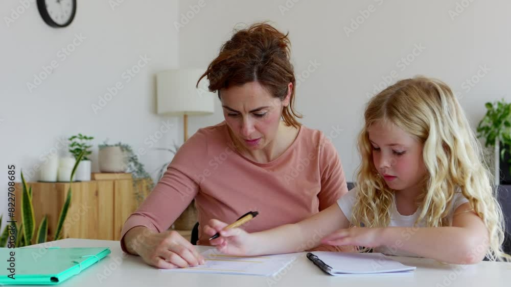 Young little cute girl doing homework with her mother at home. Young adult mother helping her daughter with school tasks. Education and family concept. Young little cute girl doing homework with her mother at home. Young adult mother helping her daughter with school tasks. Education and family concept.