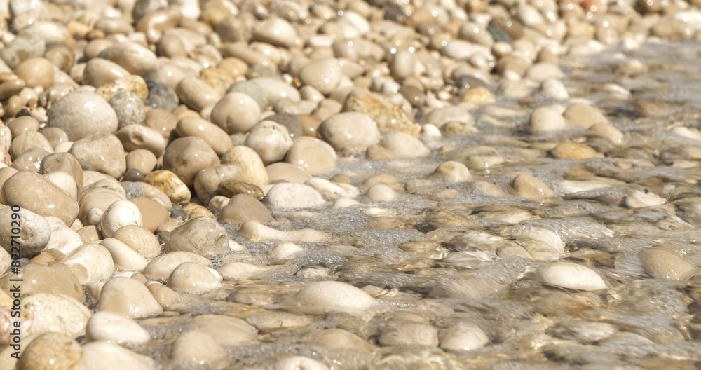 CLOSE UP: Small sea waves gently splash against shore covered with white pebbles. Soothing summer scenery with crystal clear water spilling over stones. Mesmerizing and meditative feel from the beach. CLOSE UP: Small sea waves gently splash against shore covered with white pebbles. Soothing summer scenery with crystal clear water spilling over stones. Mesmerizing and meditative feel from the beach.