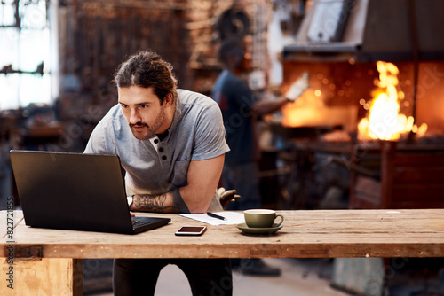 Blacksmith, factory and technology with laptop, desk and table for data analysis, email and online communication for stock. Computer, industrial and manufacturing for trade, workshop and planning