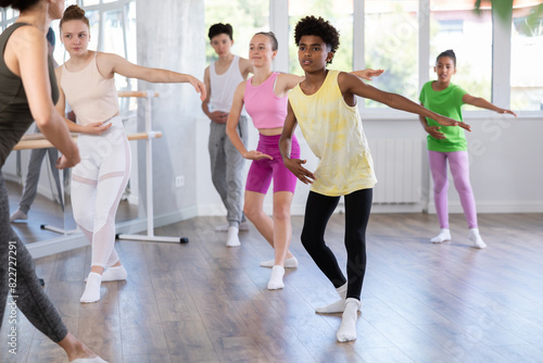 African American teenage amateur ballet dancer, dressed in yellow t-shirt and black leggings, mimicking instructor dance moves with focused precision during group class..