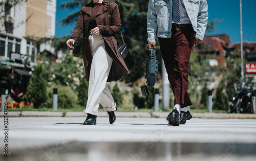 Two fashion-forward young professionals stride across a city street, showcasing modern urban style and casual elegance in their outfits.