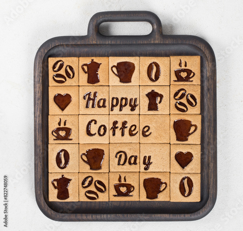 Modern coffee square cookies with a filling of coffee marmalade in the form of a picture of a cup, a heart, a coffee pot, beans, words for a happy coffee day. On a wooden plate. Top view. 