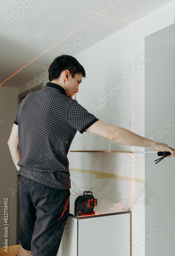 A young man checks the levelness of a shelf with a laser level. photo