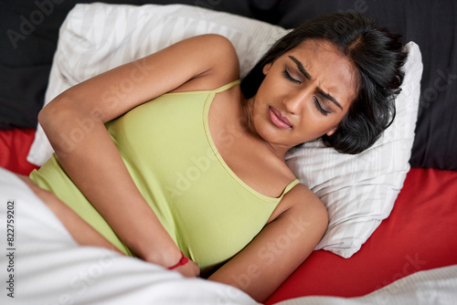 Frustrated, woman and stomach pain in bed from menstrual period with tummy cramps and stress at home. Indian, female person and medical health for abdomen agony from PMS, endometriosis and PCOS photo