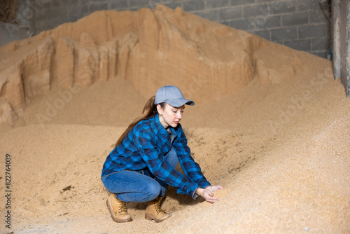 Confident young woman livestock farm owner checking soybean husk animal feed for dairy cattle in storage area..