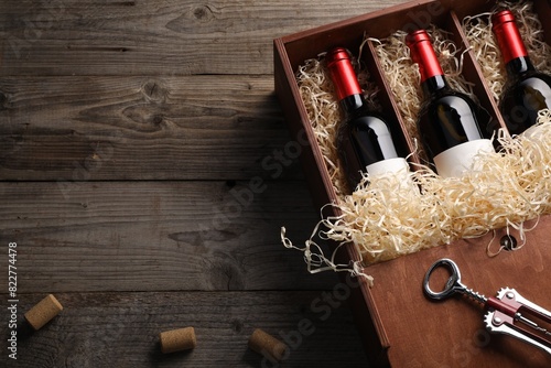 Box with wine bottles, corkscrew and corks on wooden table, flat lay. Space for text