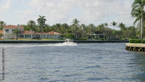 Picturesque scene with speedboat moving on water. Palm trees and colorful buildings along shore under partly cloudy sky. Leisure activities and coastal living photo