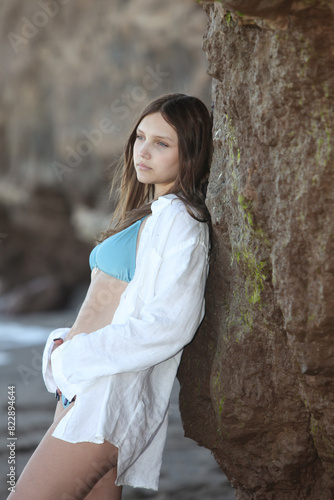 pretty girl in bikini and white shirt leaning on the rocks by the beach relaxing