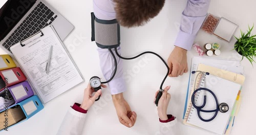Doctor measures blood pressure of male patient in clinic, top view photo