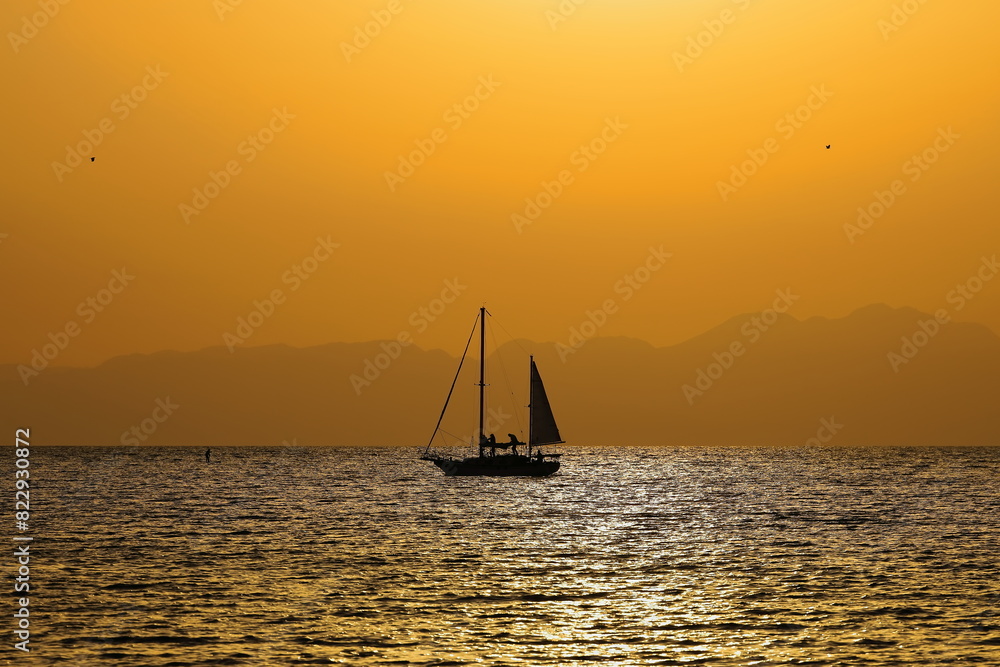 Φωτογραφία オレンジ色に染まる夕暮れの逗子海岸、優雅に浮かぶヨットのシルエット