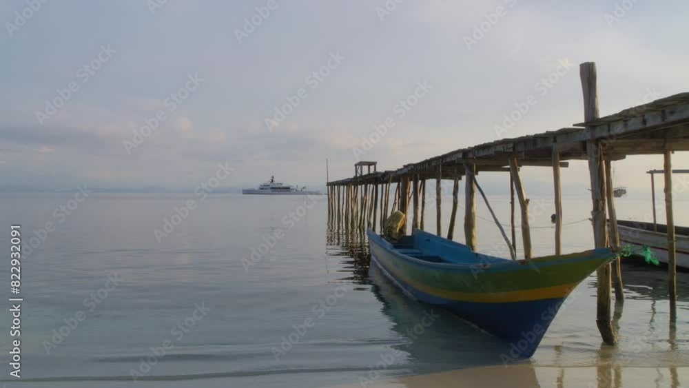 Small wooden boat anchored in Raja Ampat at jetty with luxury superyacht Wanderlust in background. Slow-motion and copy space. wealth inequality concept Small wooden boat anchored in Raja Ampat at jetty with luxury superyacht Wanderlust in background. Slow-motion and copy space. wealth inequality concept