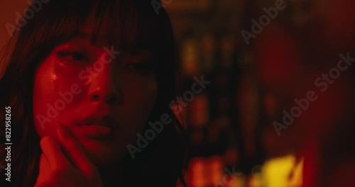 portrait of asiatic sensual passionate woman removing lipstick from her face with finger looking at the mirror of a club cafe bar with cinematic red light color photo