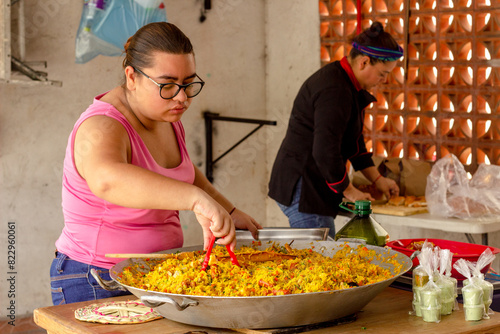 Young Latina holds tongs at small family-run Mexican paella business photo