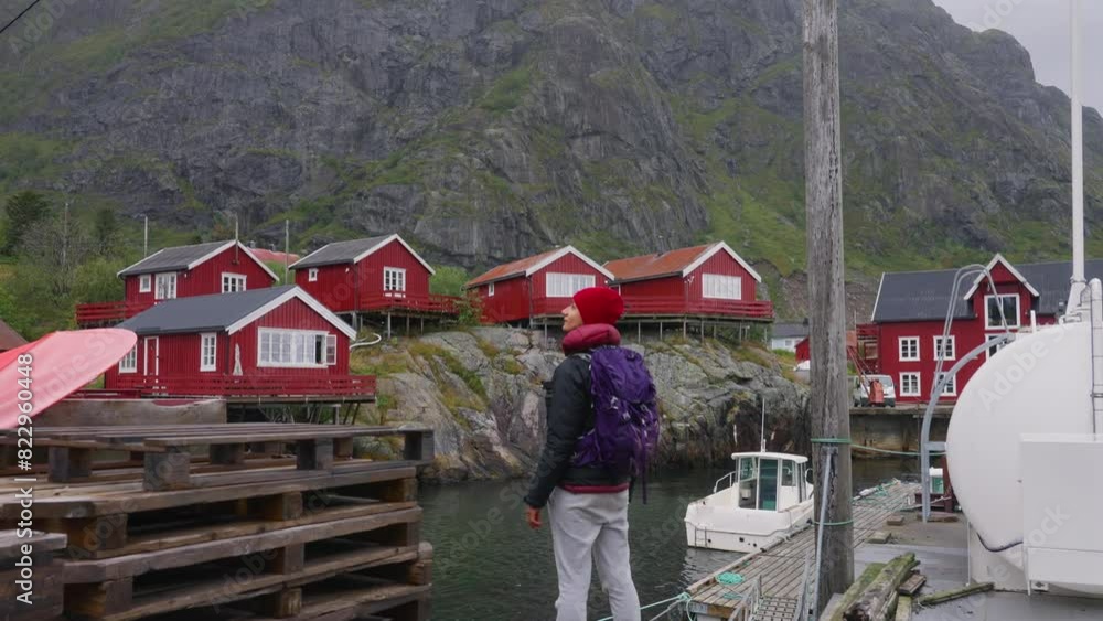 SLOW MOTION Push-out shot of a young female photographer tourist admiring the beautiful fisher village of Å and its red rorbu houses in the Lofoten Islands, Norway. SLOW MOTION Push-out shot of a young female photographer tourist admiring the beautiful fisher village of Å and its red rorbu houses in the Lofoten Islands, Norway.