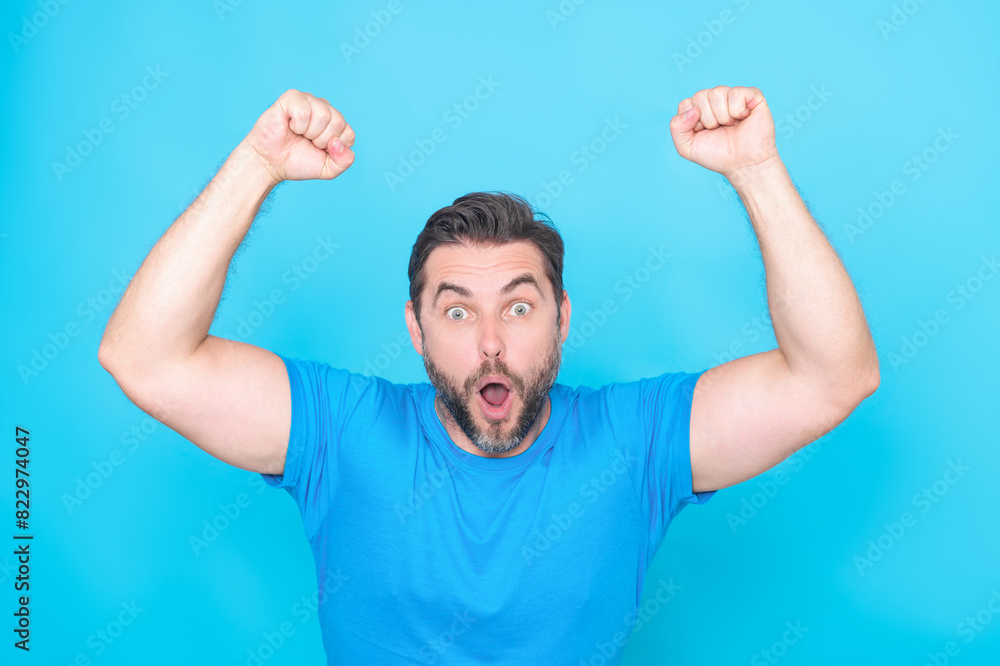 Cheerful excited man celebrating success over studio blue isolated background. Excited winner. Excited handsome man with gesture of celebration. Excited man with wow face expression. Cheerful excited man celebrating success over studio blue isolated background. Excited winner. Excited handsome man with gesture of celebration. Excited man with wow face expression.