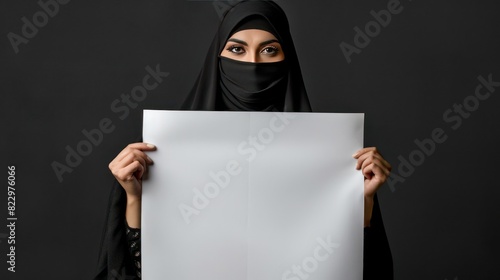An Islamic woman wearing a black niqab veil carries blank paper for a mockup text template. photo