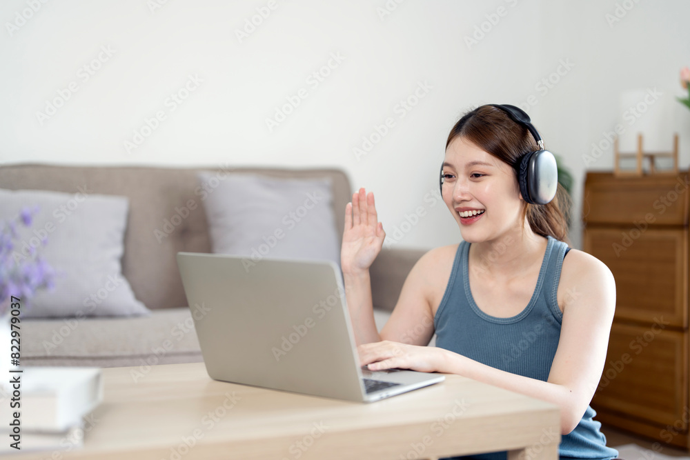 Young beautiful woman wearing headphone works for a computer from a home with a laptop sitting in living room Young beautiful woman wearing headphone works for a computer from a home with a laptop sitting in living room