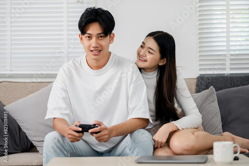 A man and woman are sitting on a couch playing a video game. The man is holding a controller and the woman is leaning on him. Scene is relaxed and playful