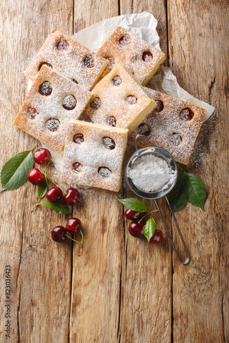 Bublanina pie fresh, juicy summer cherry enveloped in a soft sponge cake closeup on the parchment on the wooden table. Vertical top view from above photo