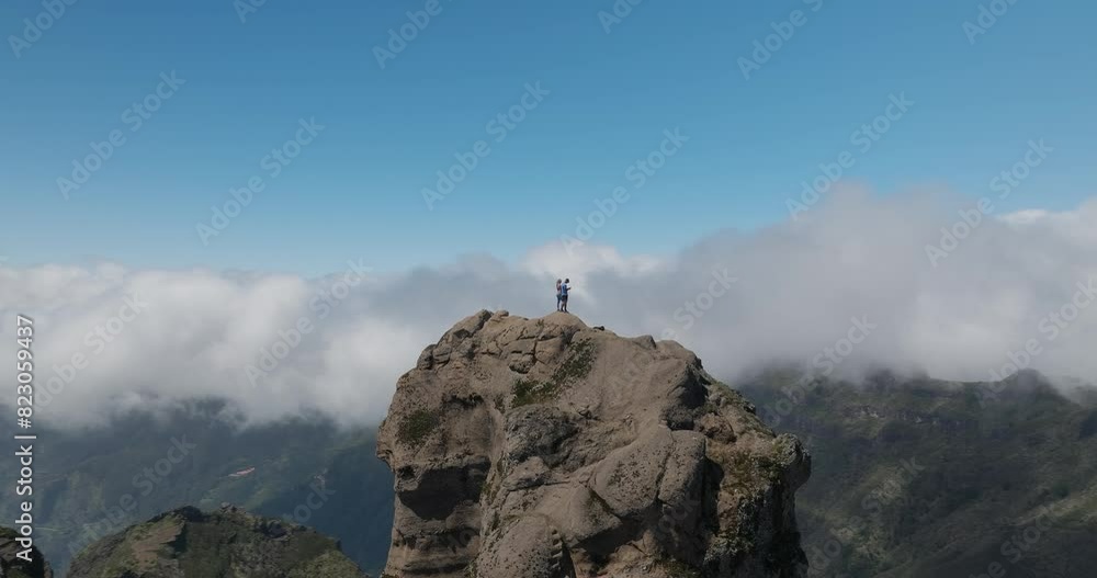 Adventure couple standing on rocky peak above clouds, rock pinnacle, orbit shot Adventure couple standing on rocky peak above clouds, rock pinnacle, orbit shot