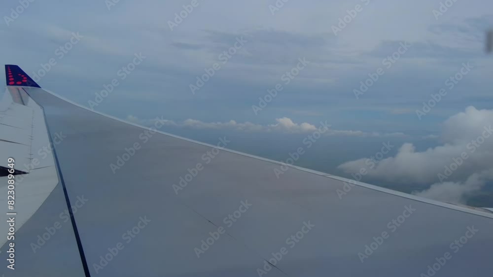 Wing of an airplane seen from window flying high above clouds with a clear sky in the background Wing of an airplane seen from window flying high above clouds with a clear sky in the background