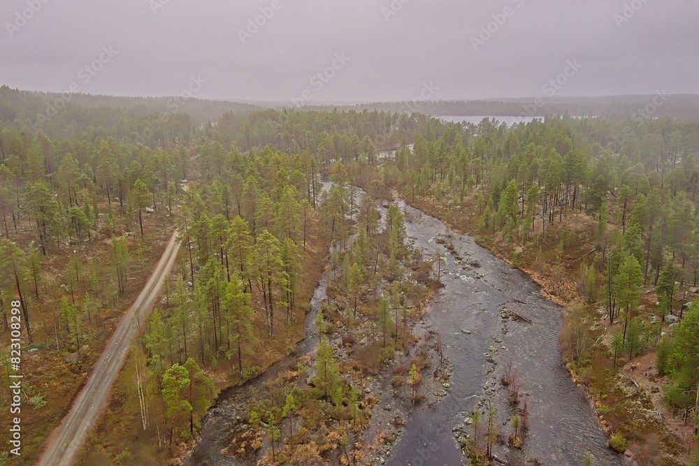 Aerial view of flowing rapids and gravel road in cloudy spring weather, Ovre Pasvik National Park, Norway.