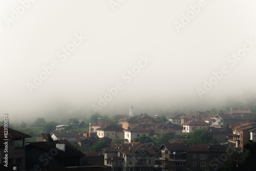 Bulgaria - 05 22 2024  Fog over a big village with small white church in the center in the background being covered in fog.