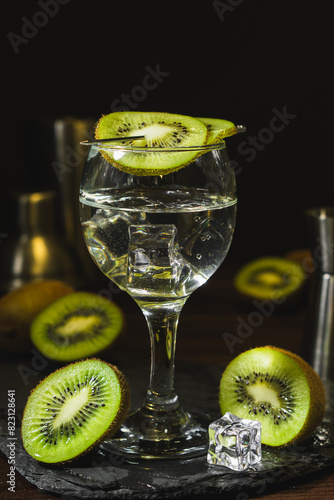 Summer cold drink and beverages. Alcohol coctail with kiwi and ice in wine glass on black background