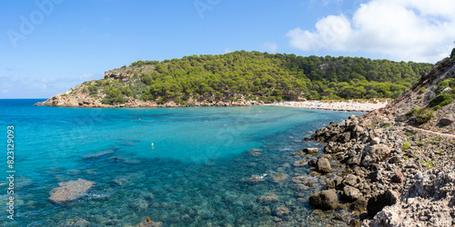 Des Bot beach on the island of Menorca next to a forest with people enjoying sunbathing and swimming