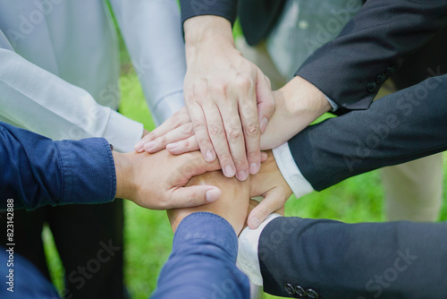 Business team unites, hands grouped in a powerful circle, embodying cooperation and strength in a green environment, symbolizing their commitment to unity and nature.