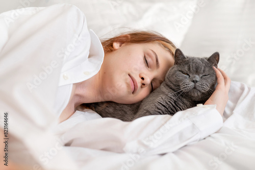 Domestic pet and child friendship and love, teenage girl laying on bed, sleeping together with gray cat, white neutral bedroom