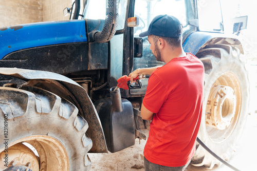 Young Farmer Refueling a Blue Tractor With a Gas Pump in a Sunny Farmyard
