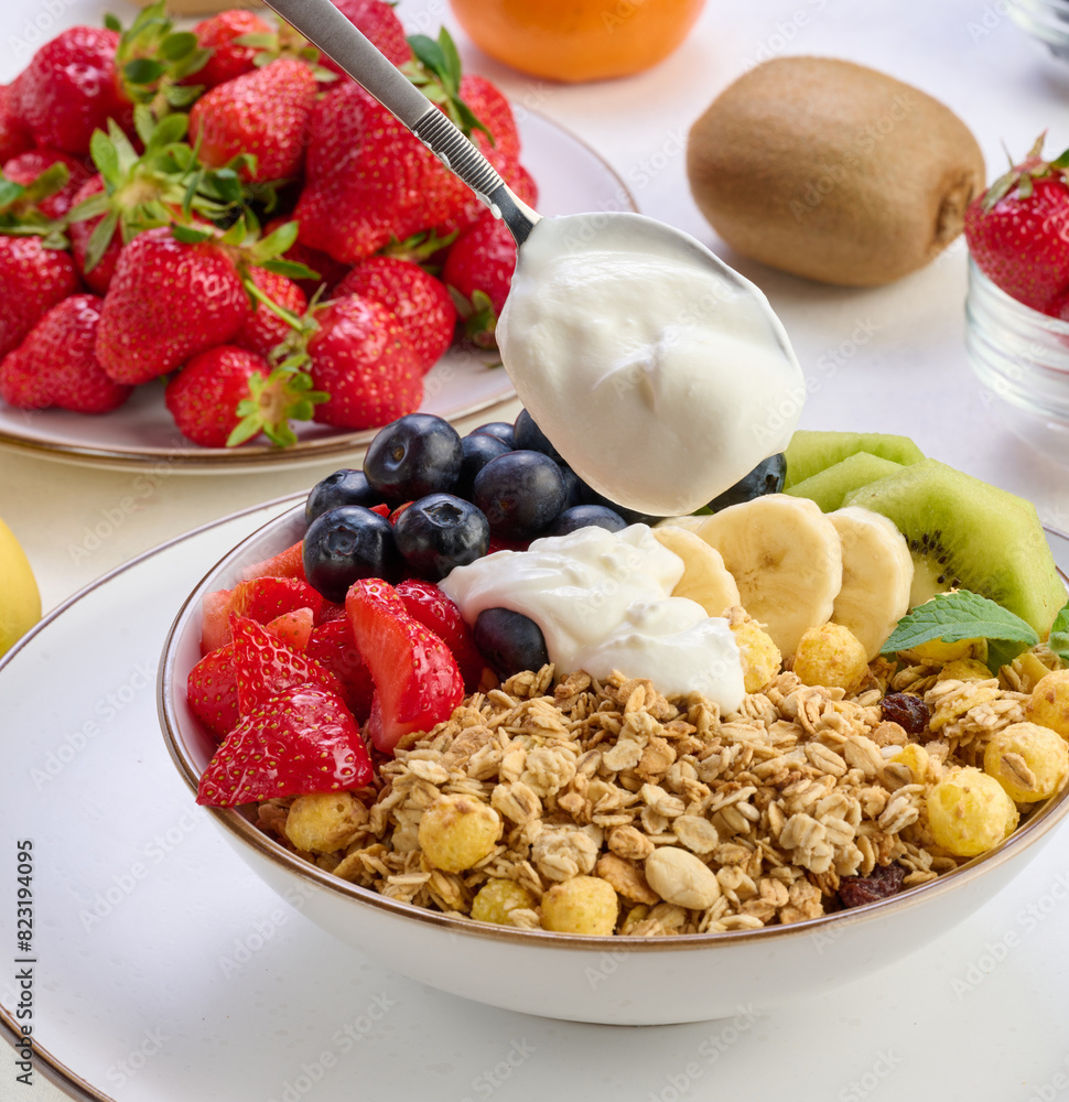 Granola with strawberries, kiwi, banana and blueberries in a round plate topped with yogurt on the table. Healthy and tasty food Granola with strawberries, kiwi, banana and blueberries in a round plate topped with yogurt on the table. Healthy and tasty food