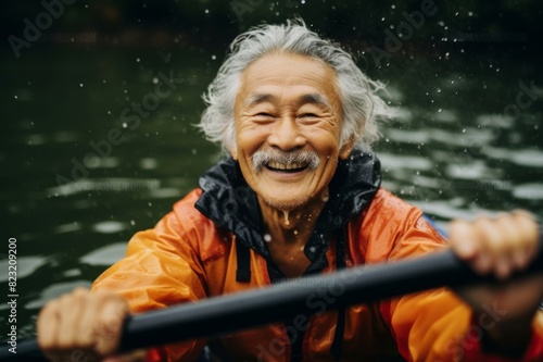 Happy senior Japanese man paddling kayak in rain © alisaaa