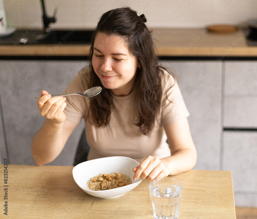 young woman holds a spoon with oatmeal and nuts in her hand, smiles young woman holds a spoon with oatmeal and nuts in her hand, smiles