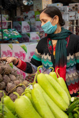 Indian mature woman wearing protective face mask and buying vegetables from outdoor market 