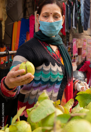 Indian mature woman wearing protective face mask and buying guava from outdoor market 