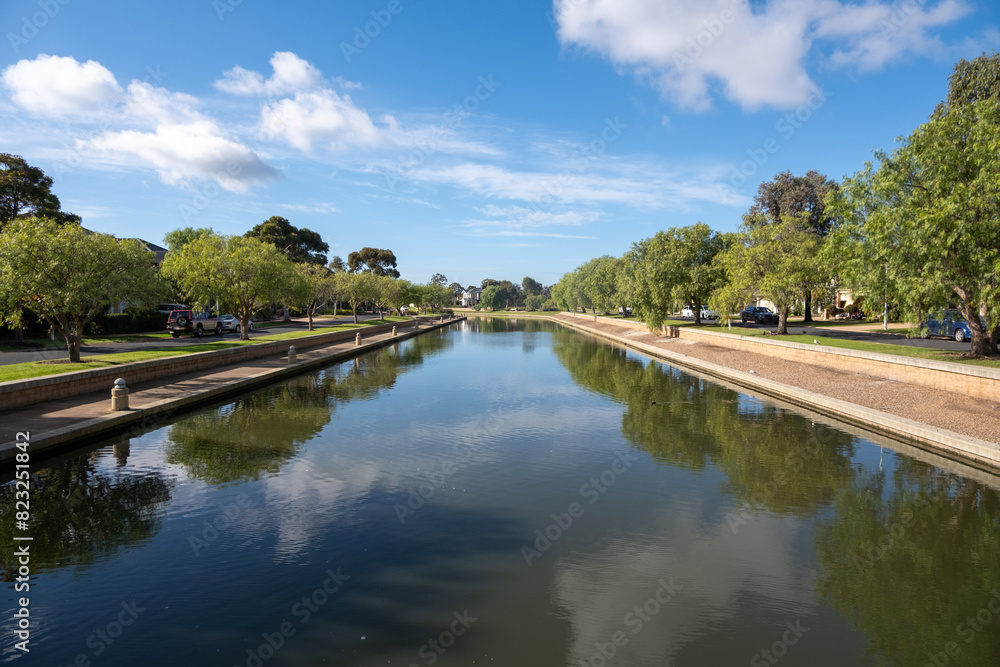 A water canal with pedestrian walkways on both sides, lined with beautiful lush green trees, in a clean and livable neighborhood. Sanctuary Lakes, Point Cook Melbourne Australia. A water canal with pedestrian walkways on both sides, lined with beautiful lush green trees, in a clean and livable neighborhood. Sanctuary Lakes, Point Cook Melbourne Australia.