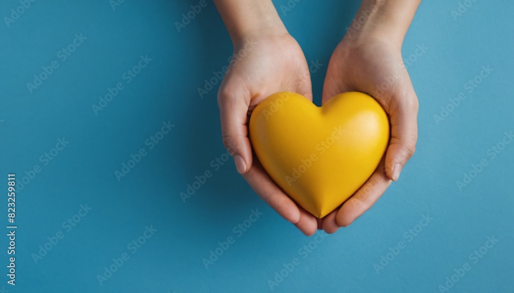 Fototapeta premium Cupped hands holding a yellow heart, minimal, blue background