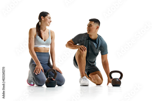 Portrait of man and woman taking break from their workout, kneeling on floor and smiling at each other against white studio background. Concept of people in sport, healthy lifestyle, teamwork. Ad