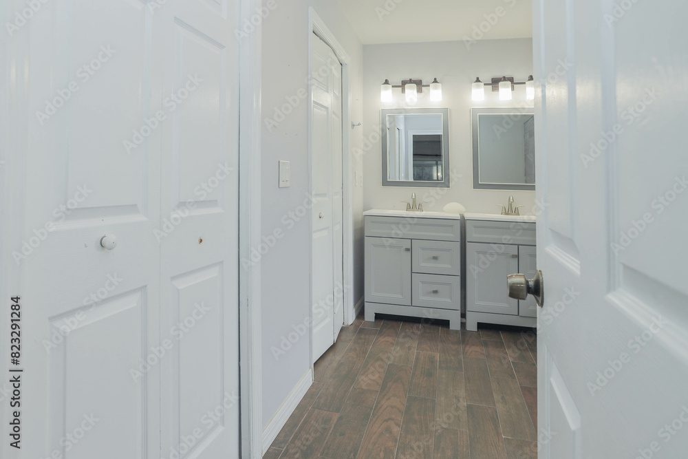 White and gray bathroom with a double sink, mirrors, and cabinets on each side White and gray bathroom with a double sink, mirrors, and cabinets on each side